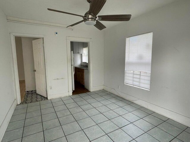 unfurnished bedroom with ceiling fan, white fridge, and light tile patterned floors