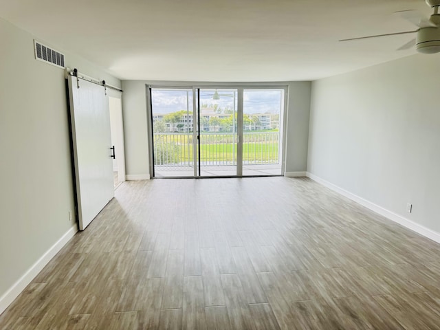 unfurnished room featuring light hardwood / wood-style floors, a barn door, and ceiling fan