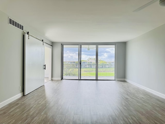 spare room with expansive windows, a barn door, ceiling fan, and light hardwood / wood-style flooring