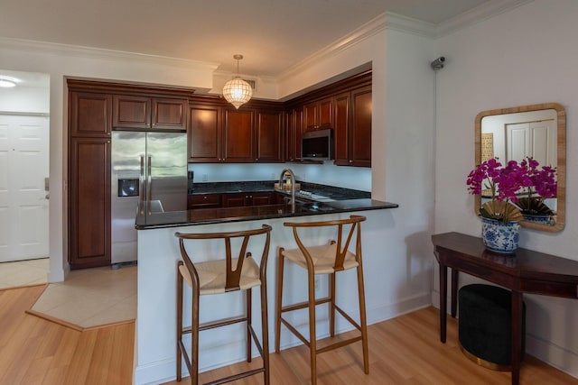 kitchen featuring stainless steel appliances, decorative light fixtures, kitchen peninsula, and light hardwood / wood-style flooring