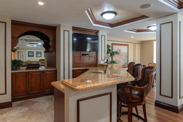 kitchen with sink, a kitchen bar, a tray ceiling, crown molding, and light stone countertops