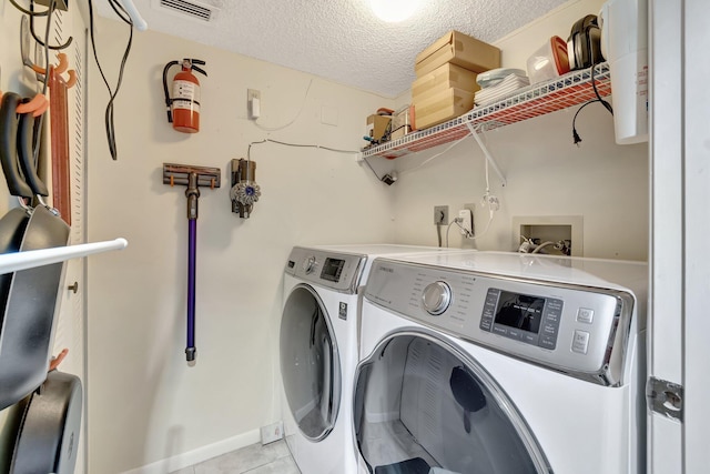 laundry area with light tile patterned floors, washer and clothes dryer, and a textured ceiling