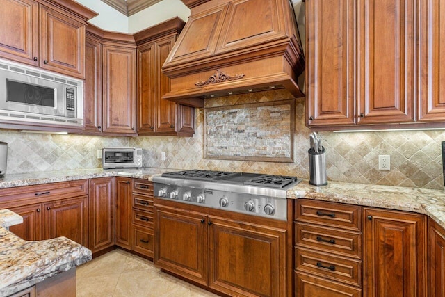 kitchen featuring tasteful backsplash, light tile patterned floors, light stone counters, stainless steel appliances, and custom range hood