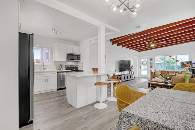 kitchen with a breakfast bar area, appliances with stainless steel finishes, white cabinetry, decorative backsplash, and kitchen peninsula