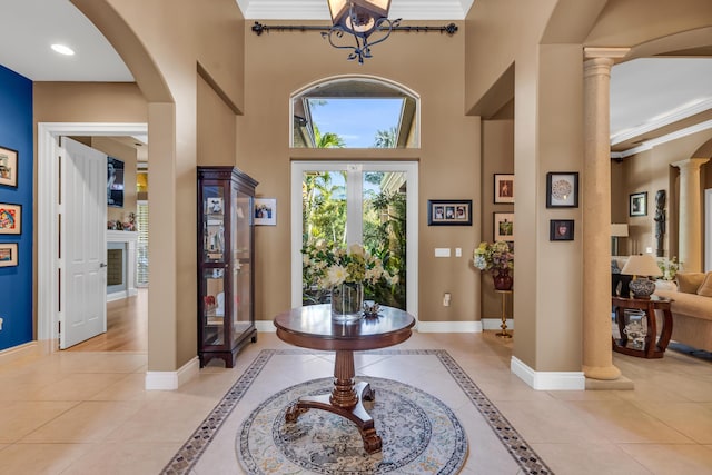 foyer entrance featuring ornate columns, ornamental molding, a high ceiling, and light tile patterned floors