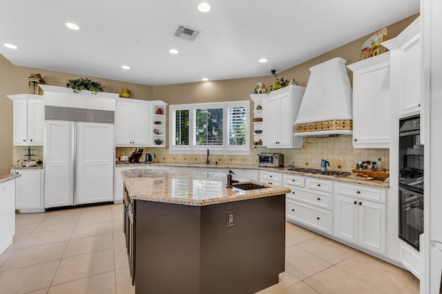 kitchen with sink, premium range hood, a kitchen island with sink, stainless steel gas cooktop, and white cabinets