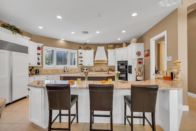 kitchen with white cabinetry, a kitchen breakfast bar, black double oven, kitchen peninsula, and custom range hood