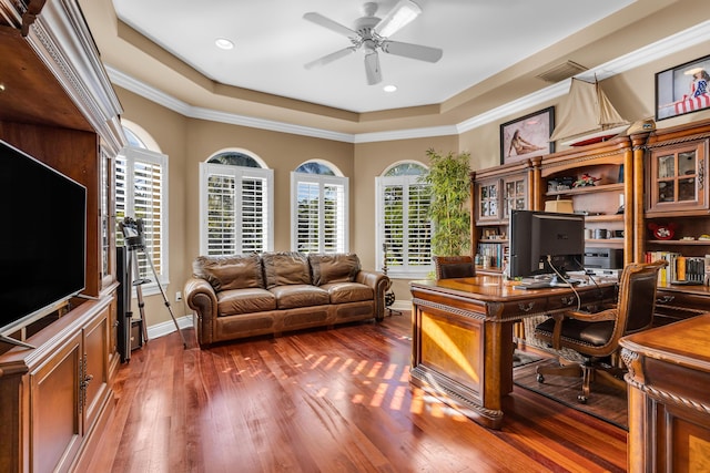 office with dark wood-type flooring, ceiling fan, crown molding, and a raised ceiling