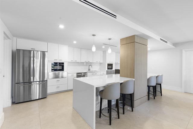 kitchen featuring a breakfast bar, a warming drawer, stainless steel appliances, light countertops, and white cabinets