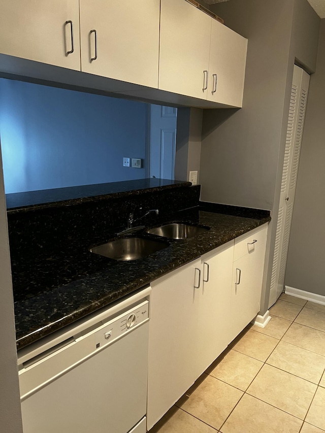 kitchen with sink, dishwasher, dark stone countertops, white cabinetry, and light tile patterned flooring