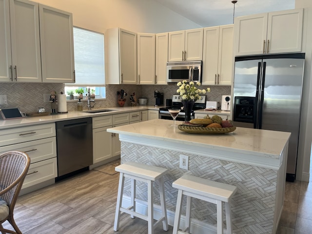 kitchen with a kitchen island, appliances with stainless steel finishes, decorative light fixtures, sink, and light stone counters