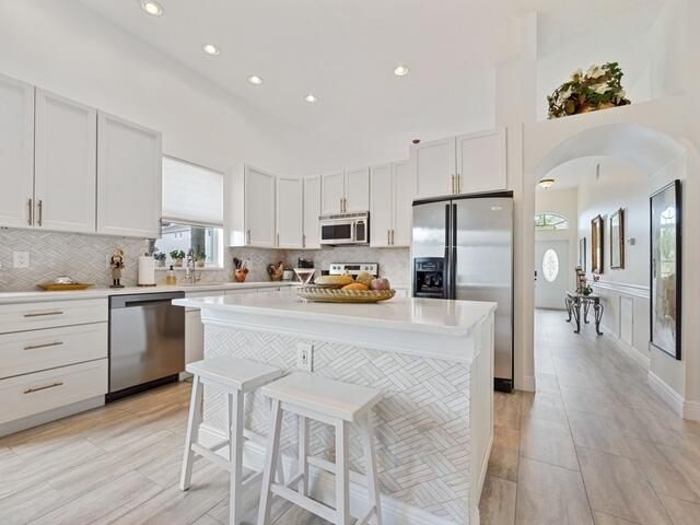 kitchen with appliances with stainless steel finishes, white cabinetry, a kitchen breakfast bar, decorative backsplash, and a center island