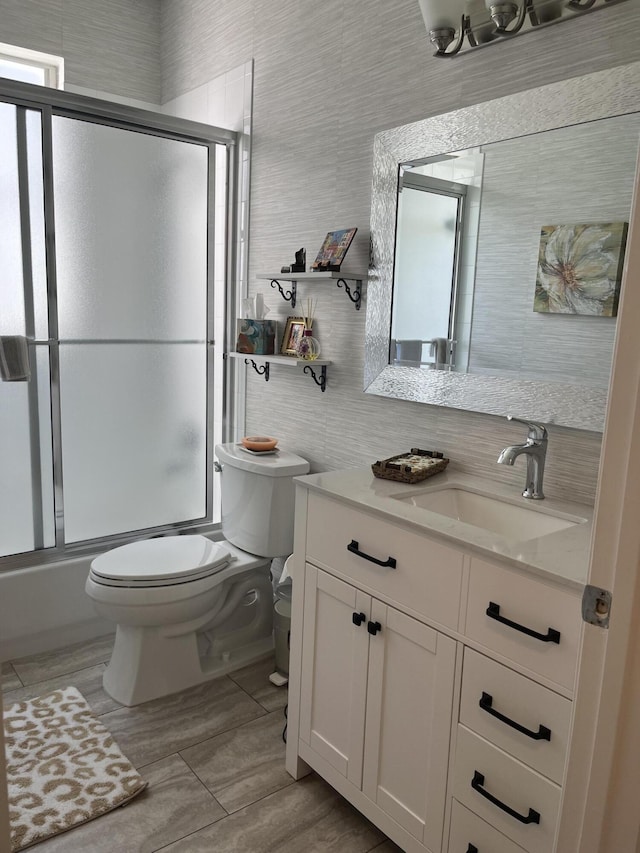 full bathroom with tile walls, vanity, bath / shower combo with glass door, and toilet