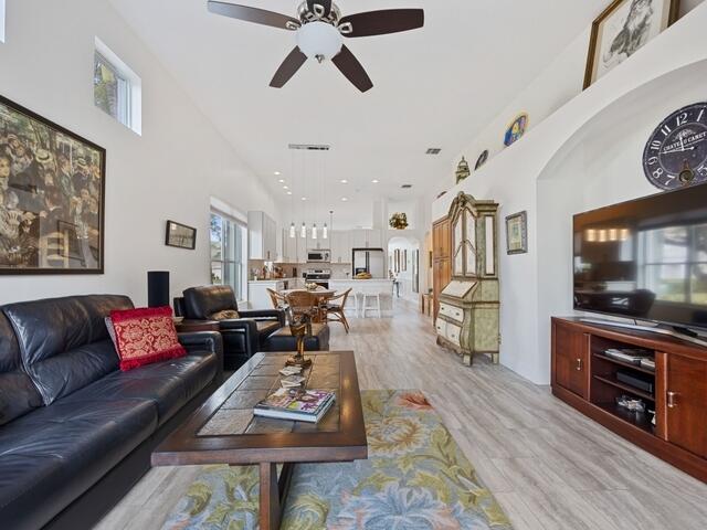 living room with a towering ceiling, light hardwood / wood-style floors, and ceiling fan