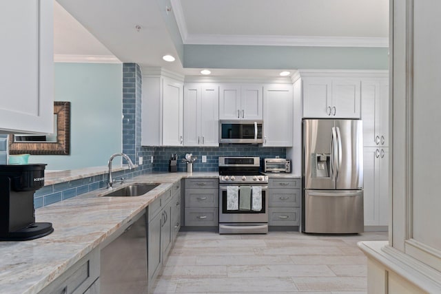 kitchen with sink, white cabinetry, light stone counters, ornamental molding, and stainless steel appliances