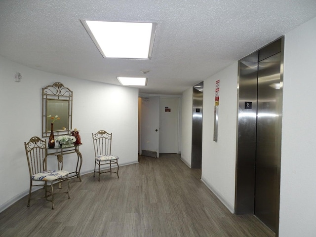 hallway with hardwood / wood-style flooring, elevator, and a textured ceiling