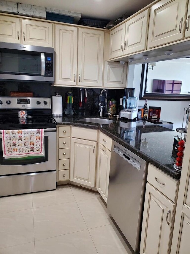 kitchen with sink, light tile patterned floors, appliances with stainless steel finishes, dark stone countertops, and decorative backsplash