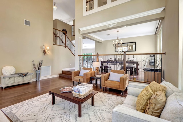 living room with wood-type flooring, ornamental molding, a chandelier, and a high ceiling