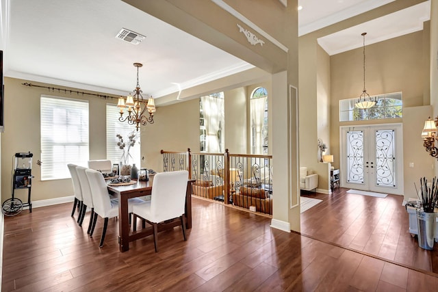 dining room featuring dark wood-type flooring, french doors, crown molding, a notable chandelier, and a towering ceiling