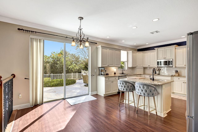 kitchen with dark wood-type flooring, light stone counters, decorative light fixtures, a center island with sink, and stainless steel appliances