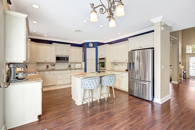 kitchen featuring stainless steel appliances, light stone countertops, pendant lighting, and a center island with sink