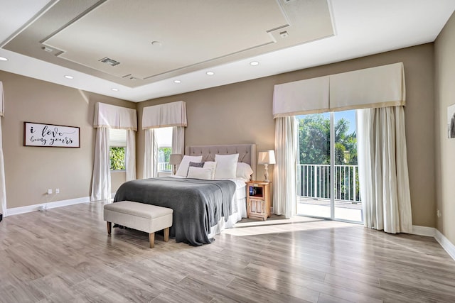 bedroom with a tray ceiling, light wood-type flooring, and access to outside