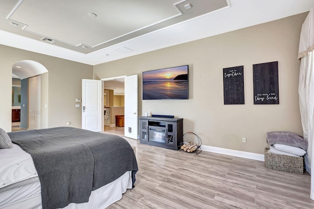 bedroom featuring connected bathroom, light wood-type flooring, and a tray ceiling