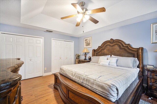 bedroom with a raised ceiling, light hardwood / wood-style floors, a textured ceiling, and two closets