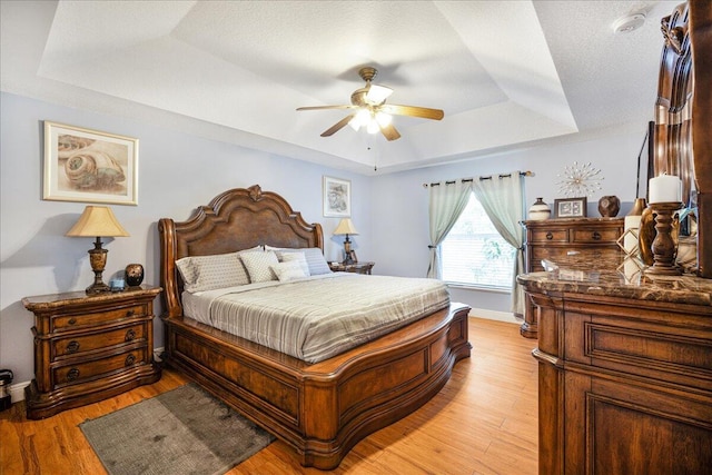 bedroom with a raised ceiling, a textured ceiling, ceiling fan, and light hardwood / wood-style flooring