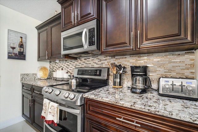 kitchen with backsplash, dark brown cabinets, light stone countertops, and appliances with stainless steel finishes