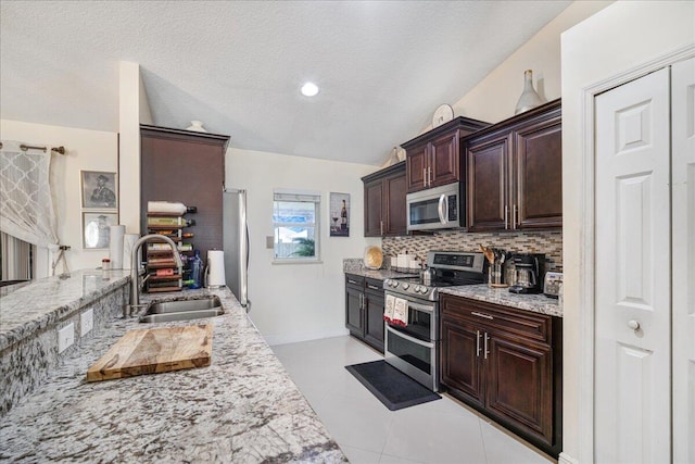 kitchen with sink, appliances with stainless steel finishes, light stone countertops, light tile patterned flooring, and decorative backsplash