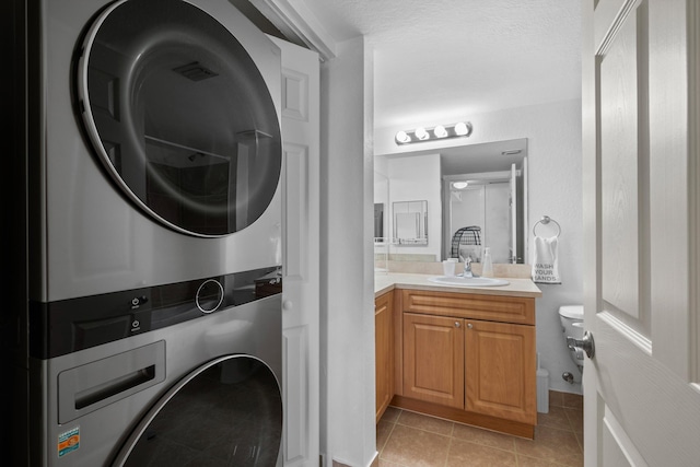 clothes washing area with stacked washer and dryer, sink, and light tile patterned floors