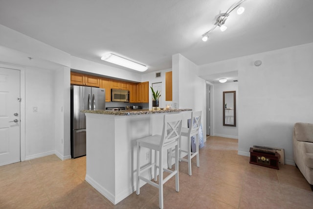 kitchen with light stone countertops, appliances with stainless steel finishes, a breakfast bar area, and kitchen peninsula