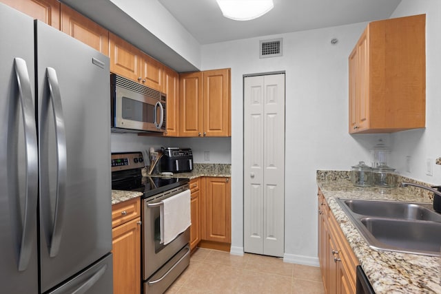 kitchen with stainless steel appliances, light tile patterned flooring, sink, and light stone counters