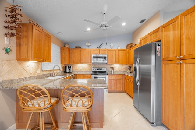 kitchen featuring sink, light tile patterned floors, a breakfast bar, appliances with stainless steel finishes, and kitchen peninsula