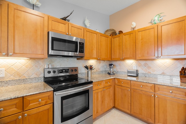 kitchen featuring decorative backsplash, light stone counters, light tile patterned floors, and stainless steel appliances
