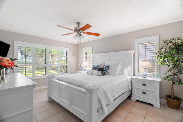 bedroom with ceiling fan, light tile patterned floors, baseboards, and a textured ceiling