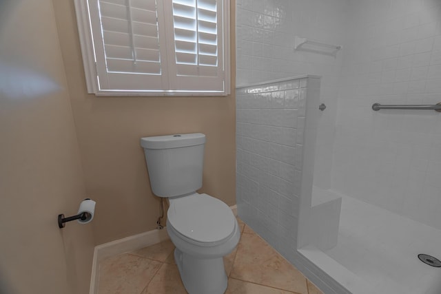 full bath with tile patterned flooring, toilet, baseboards, and tiled shower