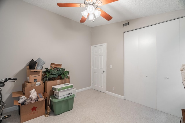 miscellaneous room featuring ceiling fan, light carpet, and a textured ceiling