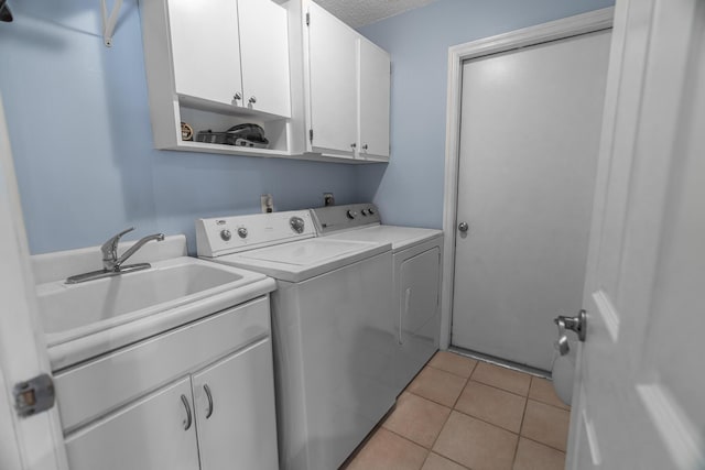 clothes washing area featuring a sink, a textured ceiling, washing machine and dryer, cabinet space, and light tile patterned floors