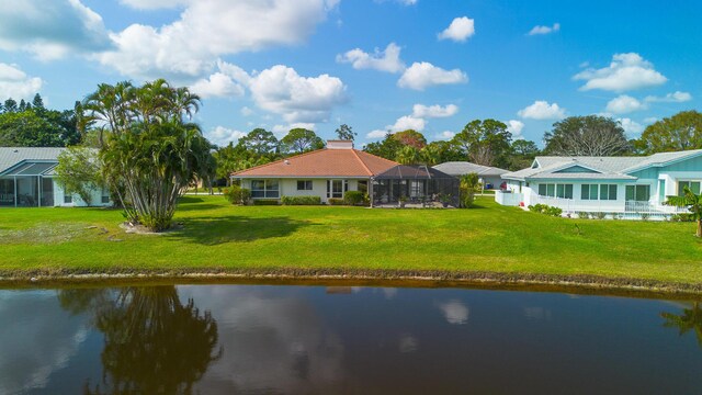 back of property with a chimney, glass enclosure, a lawn, and a water view