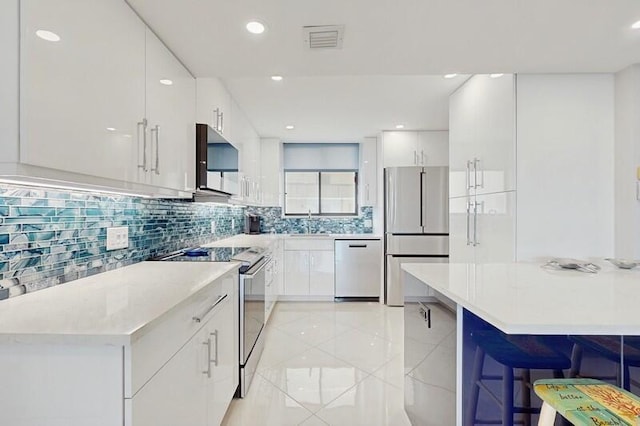 kitchen featuring appliances with stainless steel finishes, white cabinetry, sink, a breakfast bar area, and backsplash