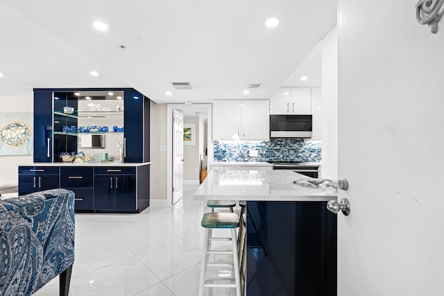 kitchen featuring stainless steel electric range, white cabinetry, a kitchen bar, light tile patterned flooring, and decorative backsplash