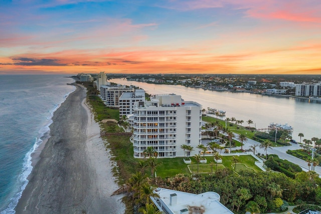 aerial view at dusk featuring a water view and a beach view