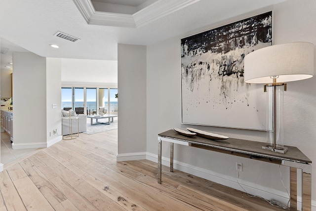 hallway featuring a raised ceiling, crown molding, and light hardwood / wood-style floors