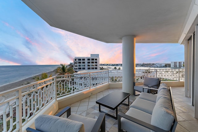 balcony at dusk featuring an outdoor living space, a water view, and a beach view