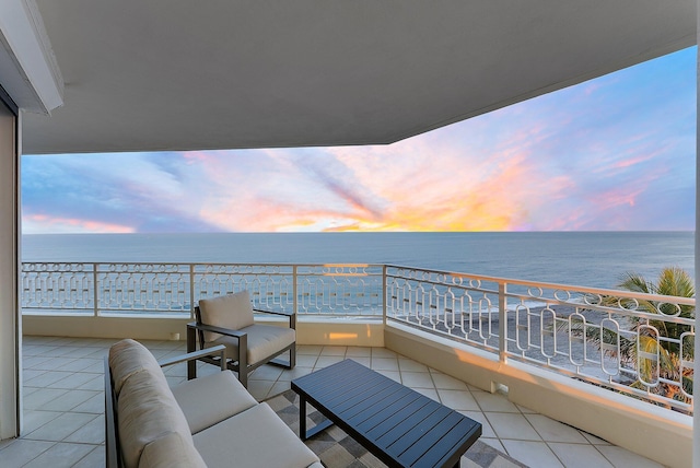 balcony at dusk with an outdoor living space, a water view, and a view of the beach