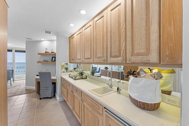 kitchen with sink, light tile patterned floors, a water view, built in desk, and light brown cabinetry