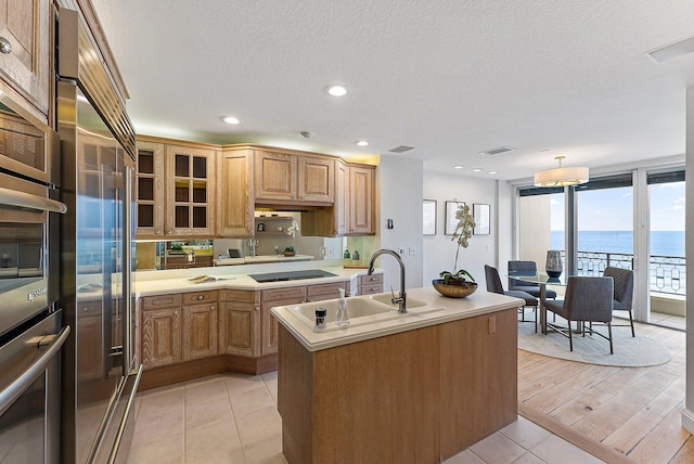 kitchen with sink, a water view, stainless steel oven, a center island with sink, and black electric cooktop