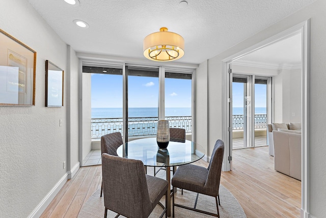 dining area with a water view, a textured ceiling, and light hardwood / wood-style flooring